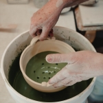 A ceramic artist dipping a bowl into a coloured glaze.