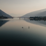 Aerial view of two people paddling on Kootenay Lake with the Big Orange Bridge in the background