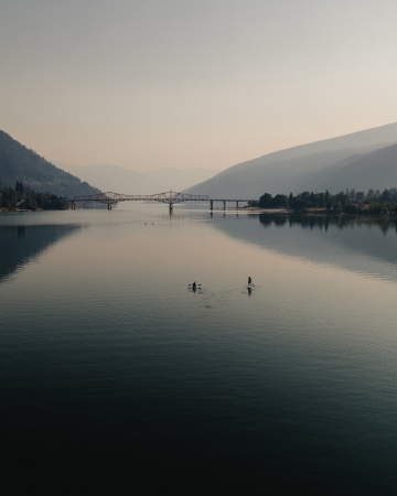 Aerial view of two people paddling on Kootenay Lake with the Big Orange Bridge in the background